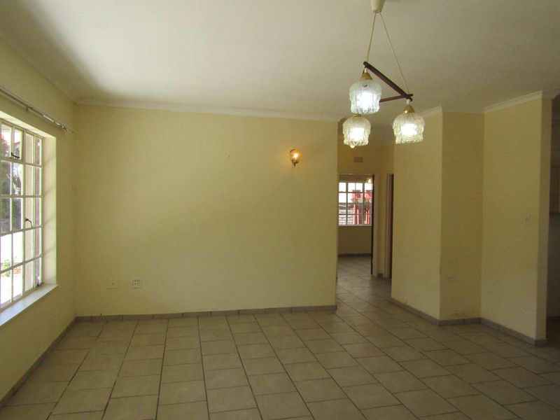 A spacious, empty living area featuring neutral tiled flooring, coved cornicing, and classic pendant lighting, offering a blank canvas for personalization.