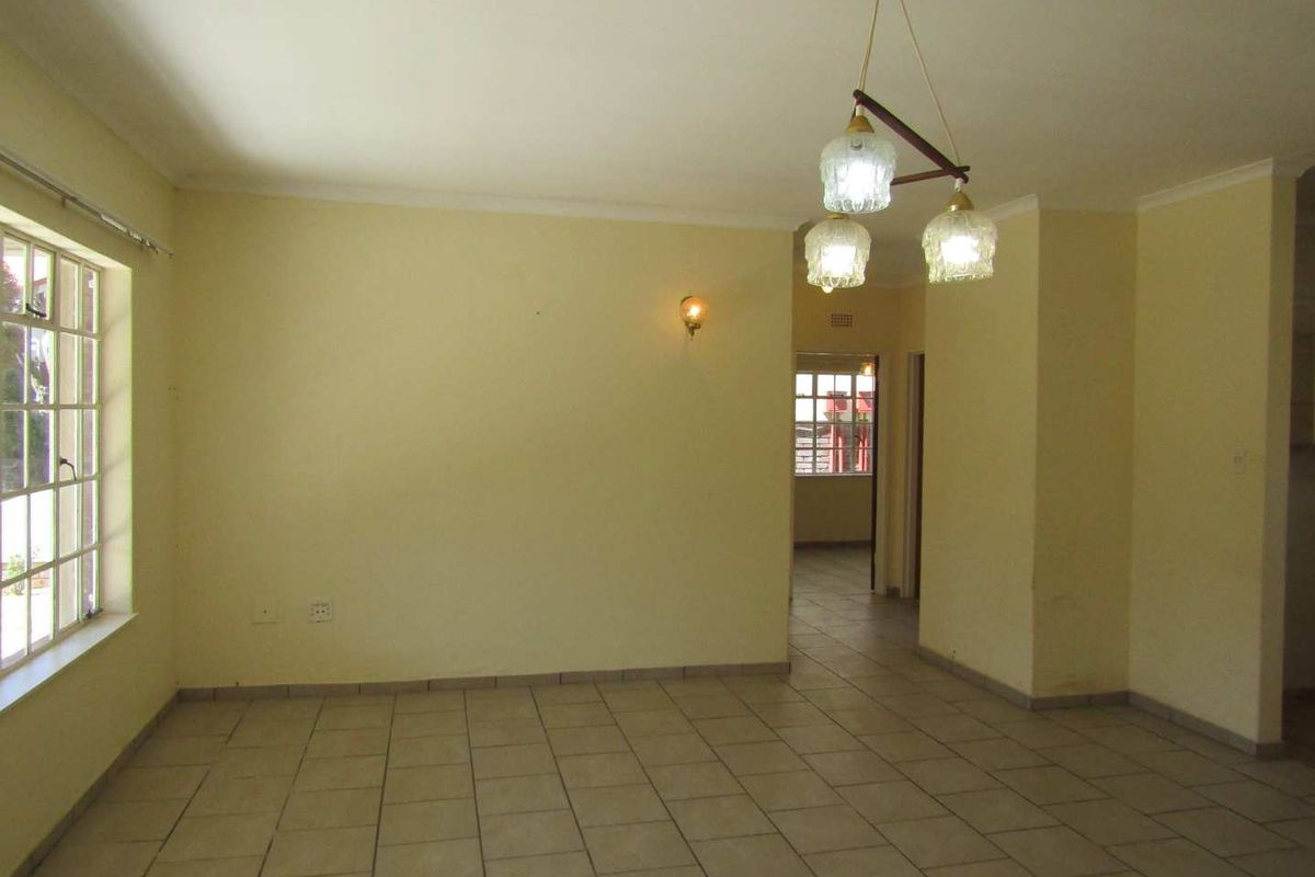 A spacious, empty living area featuring neutral tiled flooring, coved cornicing, and classic pendant lighting, offering a blank canvas for personalization.