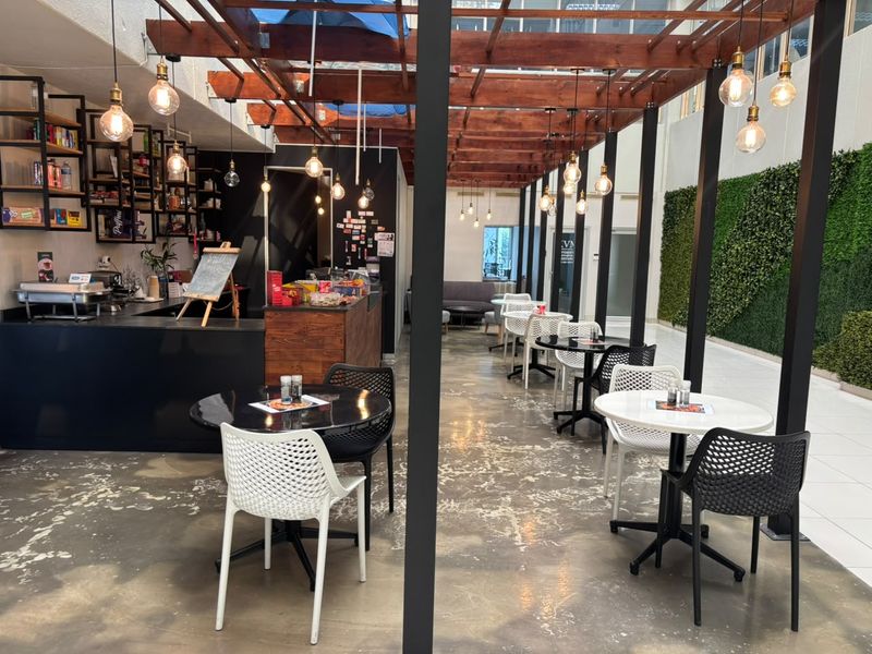 Open-plan office breakout area featuring a timber pergola, polished concrete floors, a vertical garden wall, and a built-in service counter.