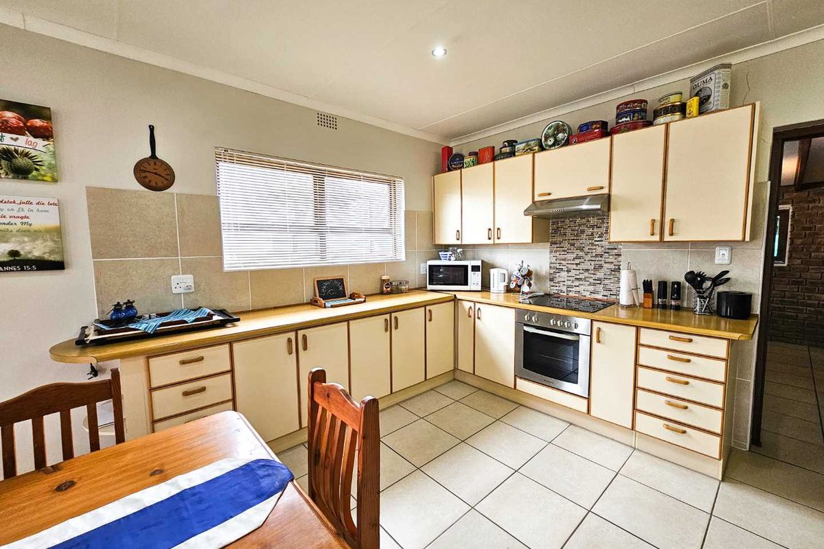 Functional kitchen featuring light-toned cabinetry, tiled backsplash, built-in oven, hob, and extractor fan with tiled flooring.