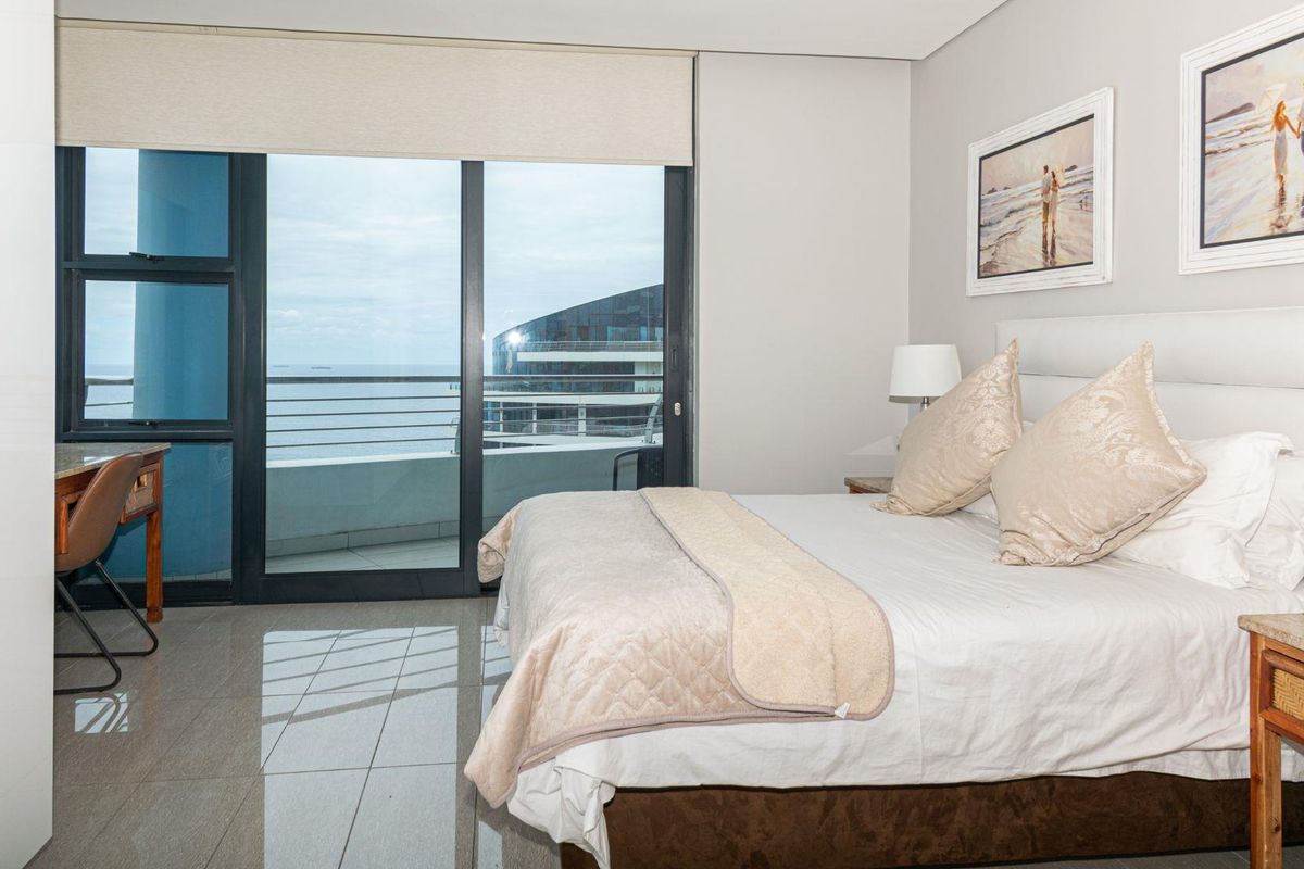 A bright bedroom featuring tiled flooring, a built-in wardrobe, and a large sliding glass door providing access to a balcony with ocean views.