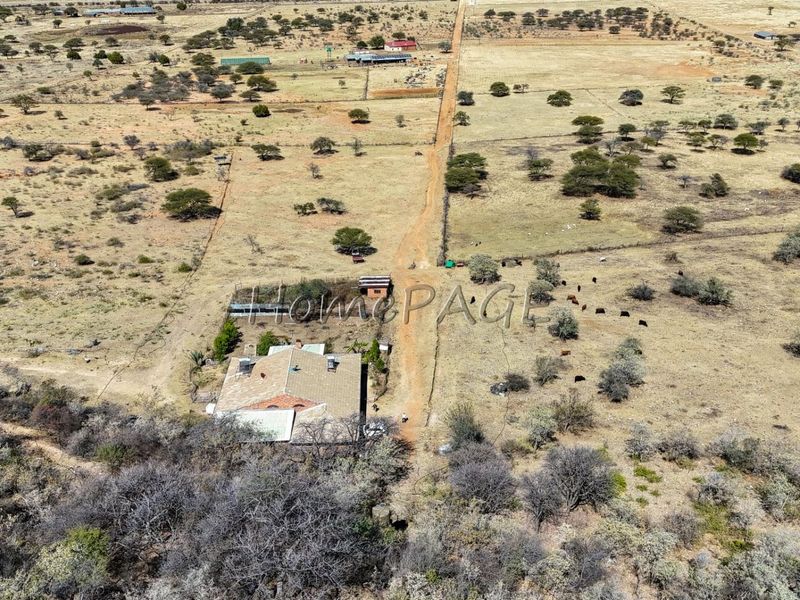 Aerial view of a small holding property featuring a main dwelling, outbuildings, fenced paddocks, and an access road set within a rural landscape.
