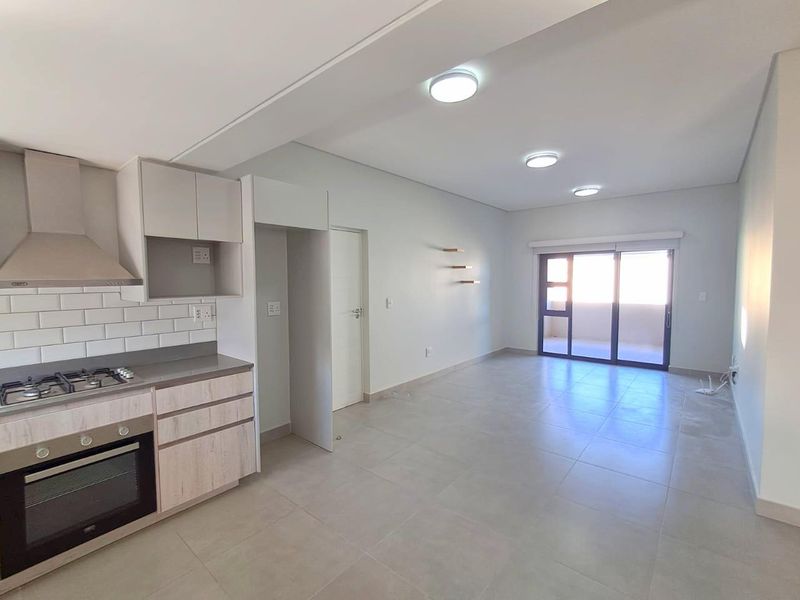 Modern open-plan kitchen and living area featuring neutral tiled floors, built-in cabinetry, integrated appliances, and sliding door access to a balcony.