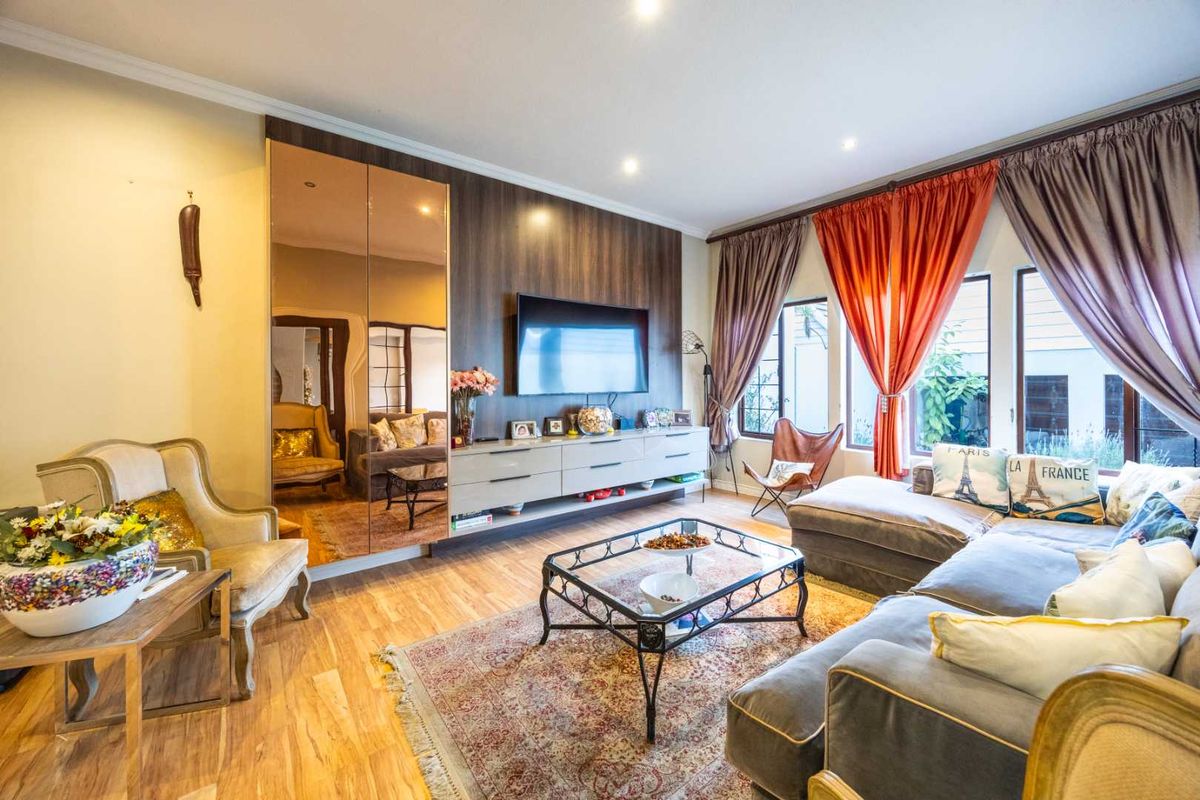 A well-maintained living room featuring hardwood flooring, recessed lighting, and a custom built-in media console with integrated mirrored wall paneling.