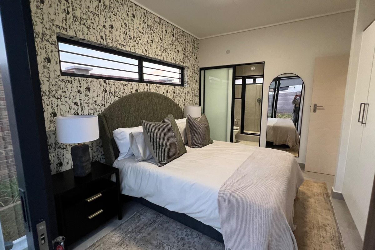 Modern bedroom featuring a patterned accent wall, clerestory windows, built-in wardrobe, and an en-suite bathroom with a sliding glass door.