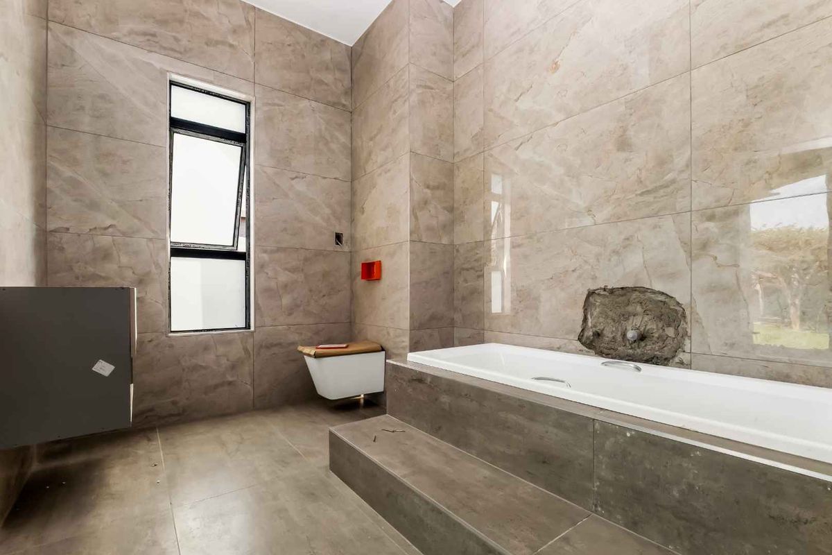 A modern bathroom featuring large-format beige tiles, a built-in bathtub, and a wall-mounted toilet, currently requiring completion of plumbing fixtures.