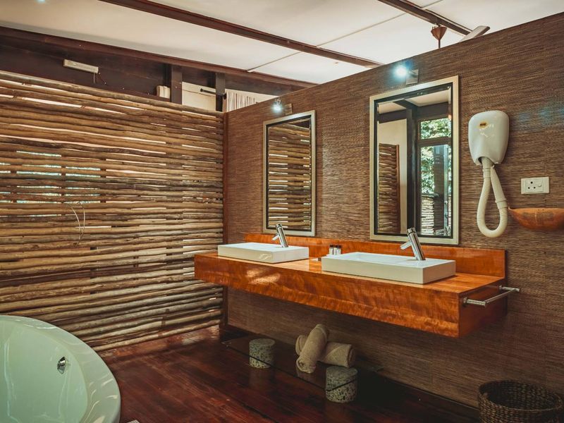 A rustic-style bathroom featuring a double vanity with vessel sinks, wall-mounted mirrors, and a freestanding bathtub set against natural timber wall finishes.