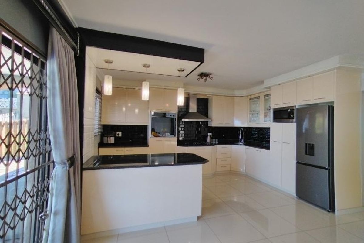 Modern kitchen featuring high-gloss cabinetry, granite countertops, integrated appliances, and tiled flooring, offering a clean and functional culinary space.