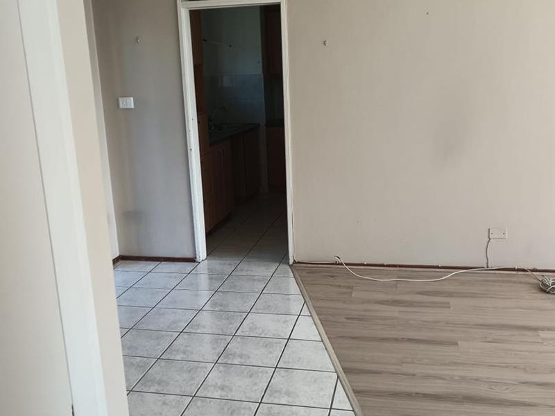An empty living area featuring a mix of tiled and laminate flooring, leading through to a kitchen space.