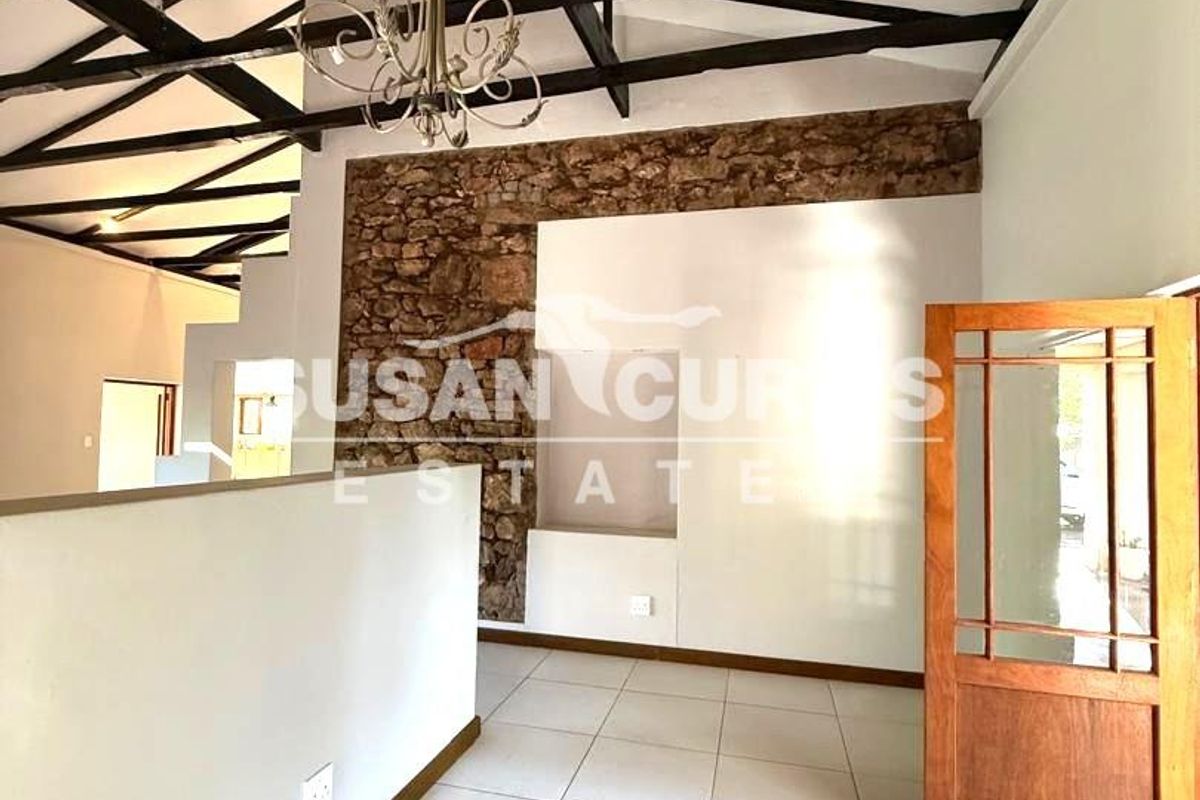 Spacious living area featuring exposed timber ceiling beams, a rustic stone feature wall, and neutral tiled flooring.