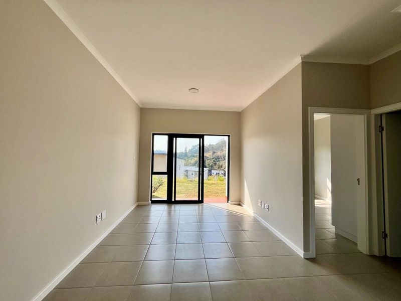 A bright, empty living room featuring neutral tiled flooring, coved cornicing, and a sliding glass door providing access to the exterior.
