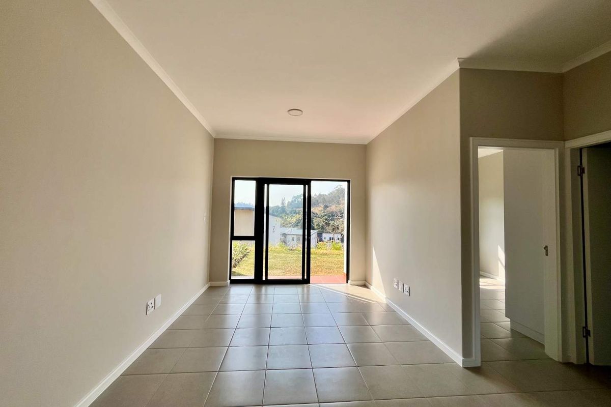 A bright, empty living room featuring neutral tiled flooring, coved cornicing, and a sliding glass door providing access to the exterior.