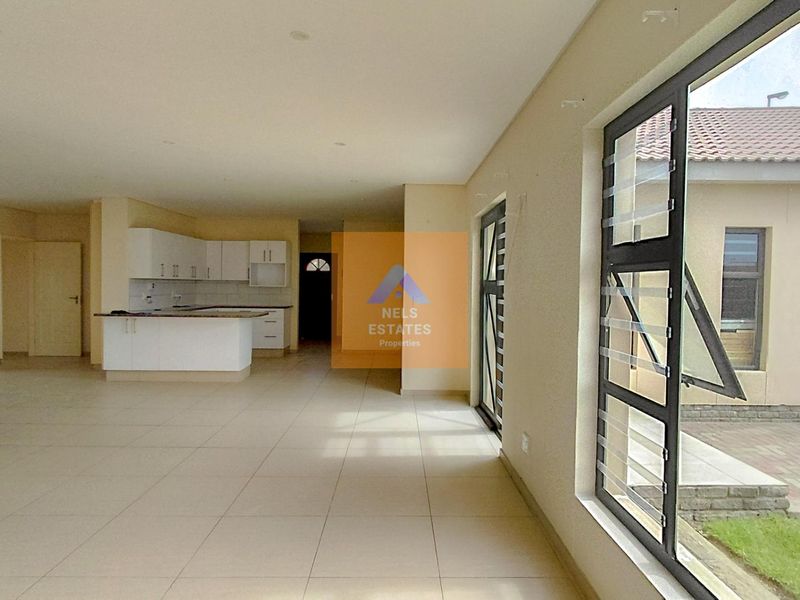 Spacious open-plan living area featuring a modern kitchen with white cabinetry, tiled floors, and large windows overlooking the exterior garden space.