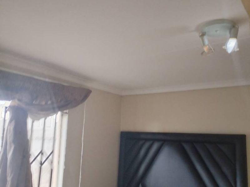 A bedroom featuring a ceiling light fixture and a window fitted with security bars.