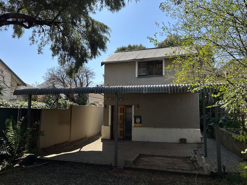 Rear exterior view of the property featuring a paved carport area, security gate, and boundary walling.