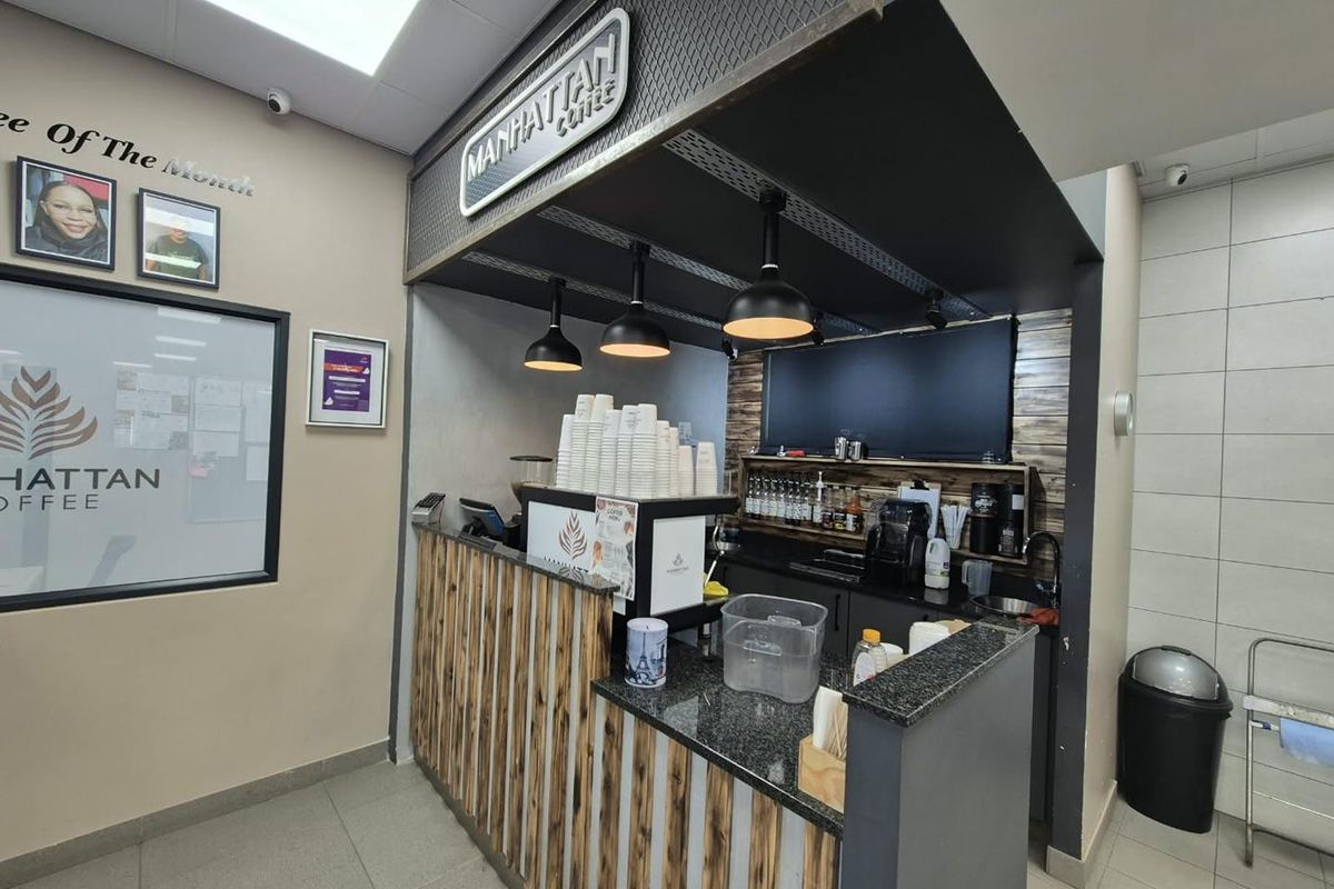 A compact commercial coffee service station featuring a granite countertop, pendant lighting, and a dedicated prep area with integrated sink and cabinetry.