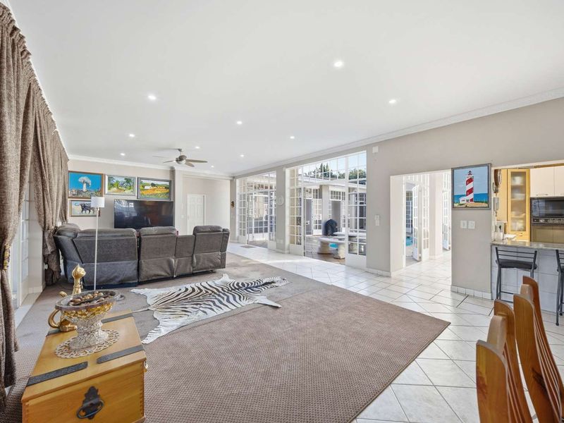 Spacious open-plan living area featuring tiled and carpeted floors, recessed lighting, and seamless access to the outdoor patio through multiple sets of french doors.