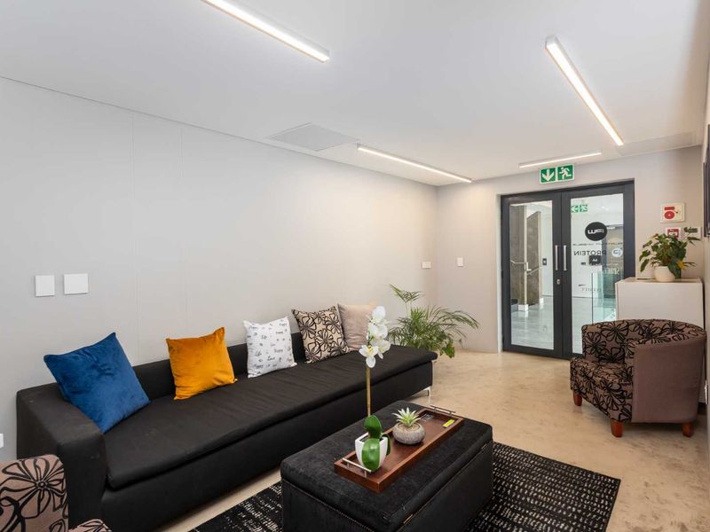 A modern, well-lit reception or waiting area featuring polished concrete floors, linear LED lighting, and a secure glass entrance door.