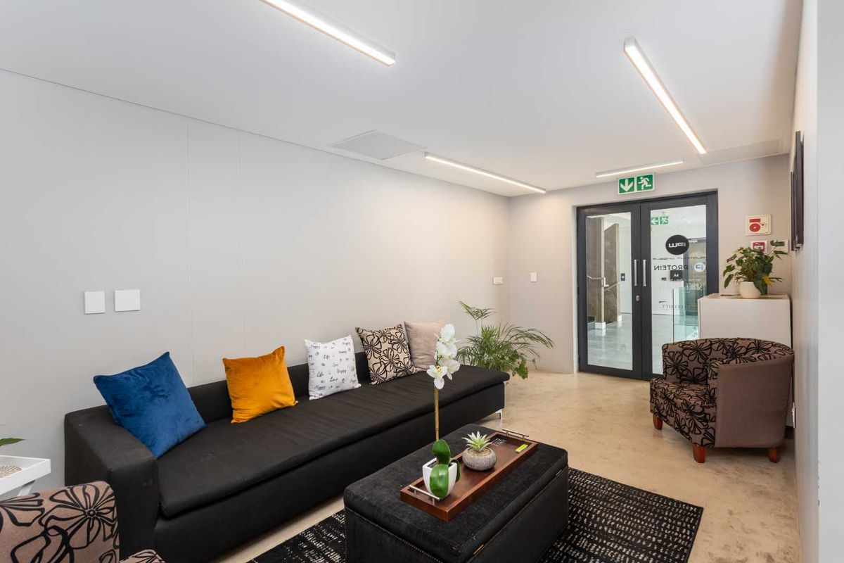 A modern, well-lit reception or waiting area featuring polished concrete floors, linear LED lighting, and a secure glass entrance door.