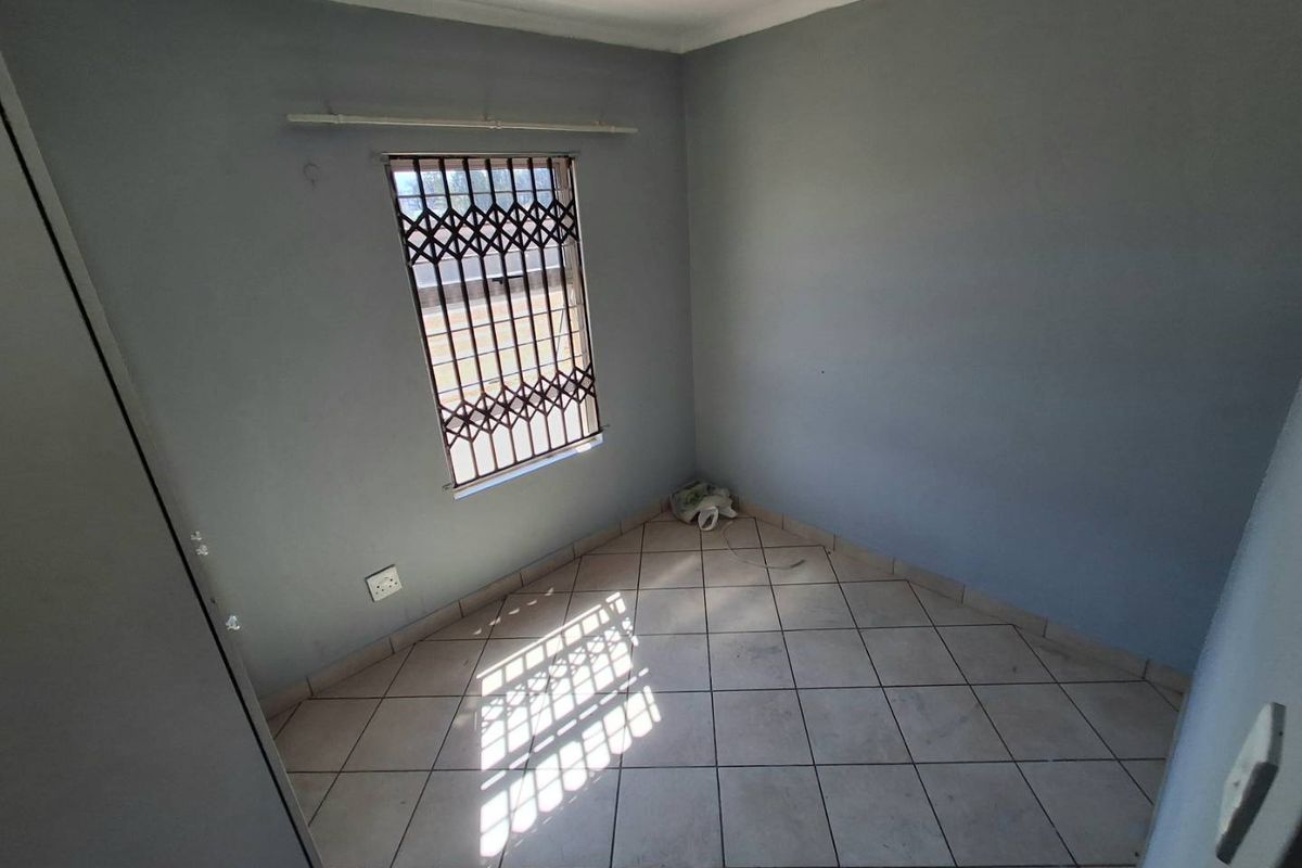 An empty bedroom featuring tiled flooring, a security gate on the window, and a built-in cupboard, ready for personalization.