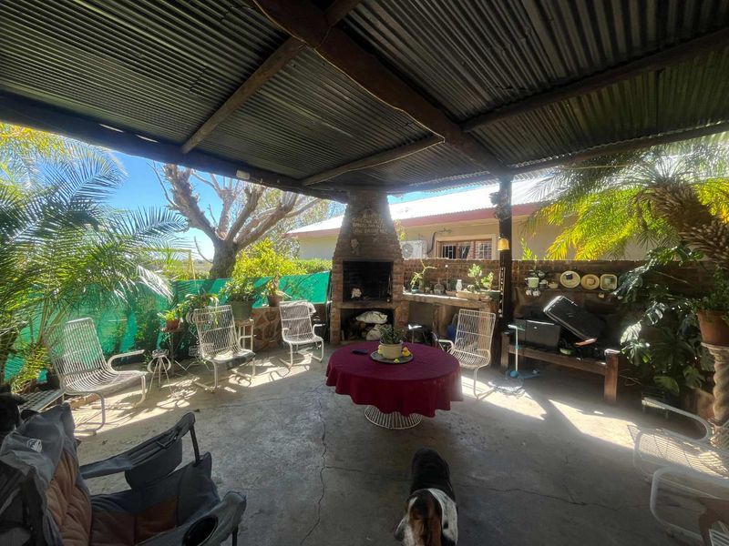 Covered outdoor patio area featuring a built-in brick fireplace, concrete flooring, and a corrugated iron roof, ideal for outdoor entertaining.