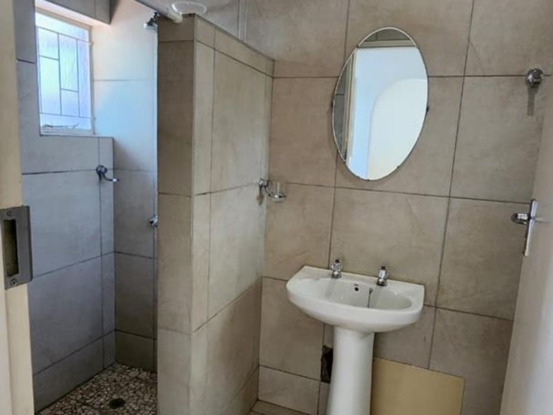 A functional bathroom featuring a pedestal basin, walk-in shower with pebble flooring, and neutral wall tiling throughout.