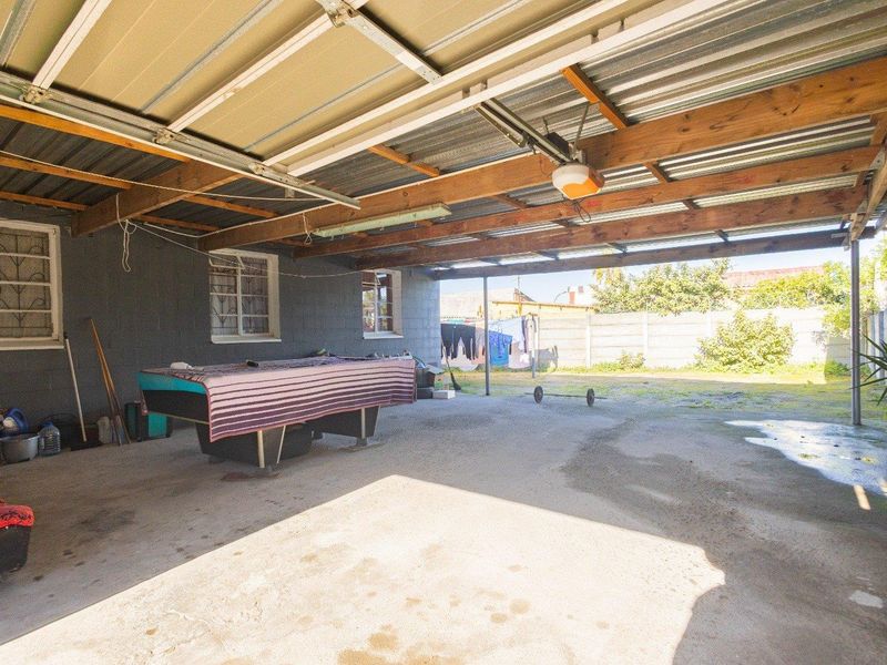 A spacious, open-sided garage or carport area featuring a concrete floor, exposed timber rafters, and a corrugated metal roof structure.