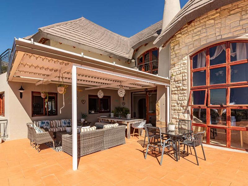 Spacious outdoor patio featuring terracotta tiling, a covered pergola area, and stone-clad exterior walls with large timber-framed windows.