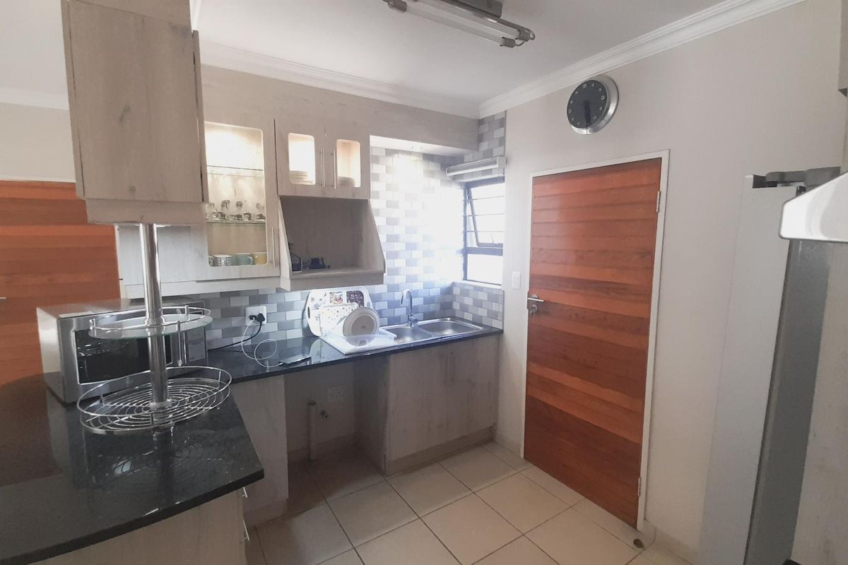 A functional kitchen featuring granite countertops, built-in cabinetry, a double sink, and tiled backsplash, providing a practical workspace with direct access to adjacent rooms.