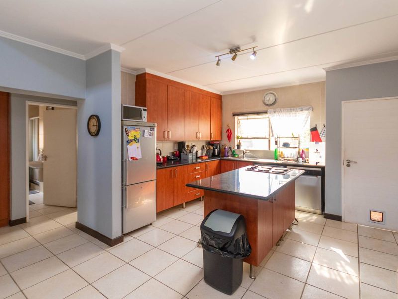 Functional kitchen featuring wooden cabinetry, granite countertops, a central island with a built-in hob, and tiled flooring.