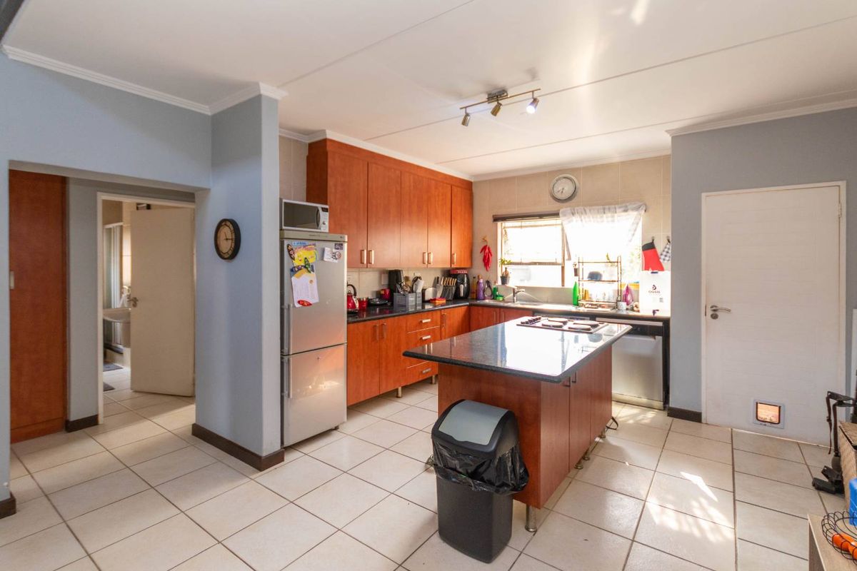 Functional kitchen featuring wooden cabinetry, granite countertops, a central island with a built-in hob, and tiled flooring.