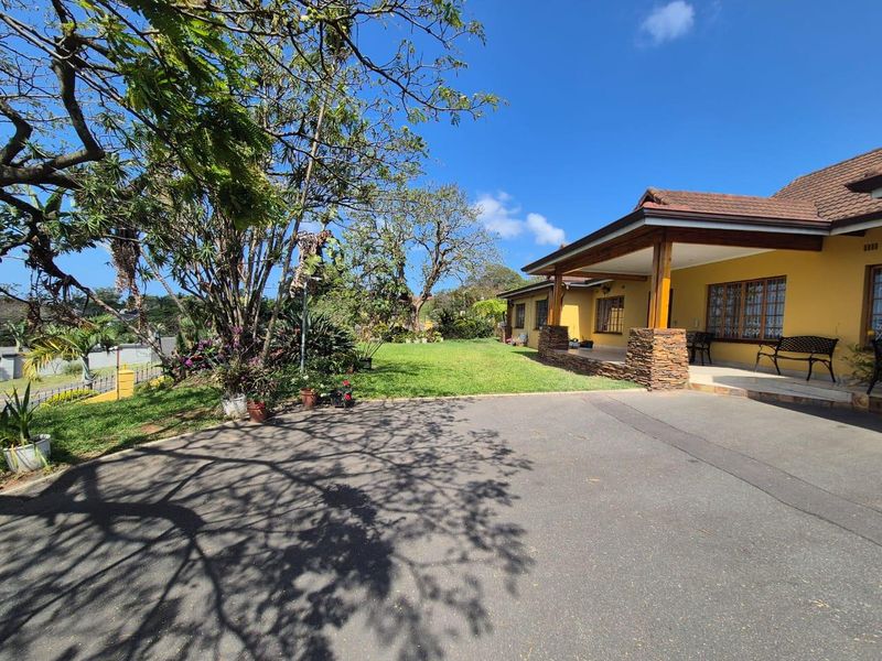 A well-maintained front exterior featuring a spacious asphalt driveway, a covered patio with stone-clad pillars, and a lush, established garden.