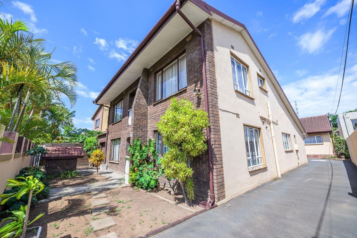 Side and rear view of a double-story brick and plastered house featuring a paved driveway and established garden area.