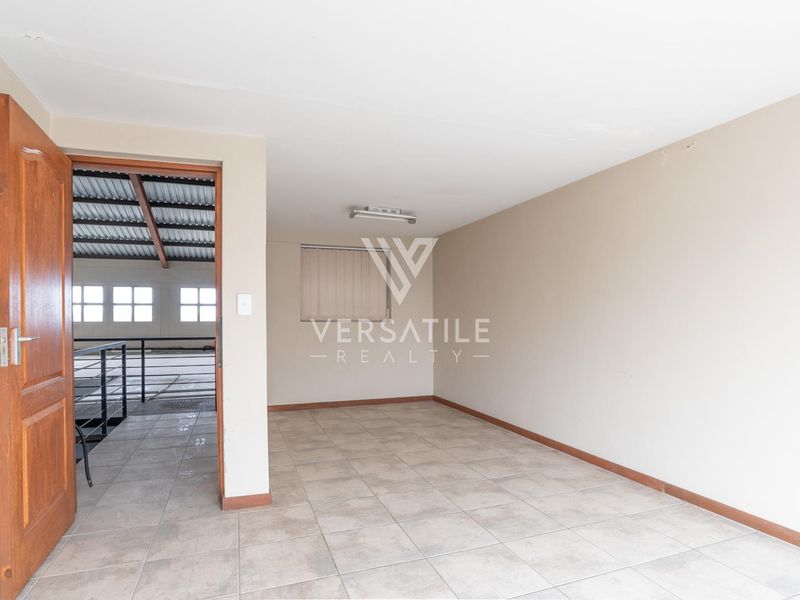 An empty office space featuring tiled flooring, neutral walls, and a doorway leading to an industrial mezzanine area.