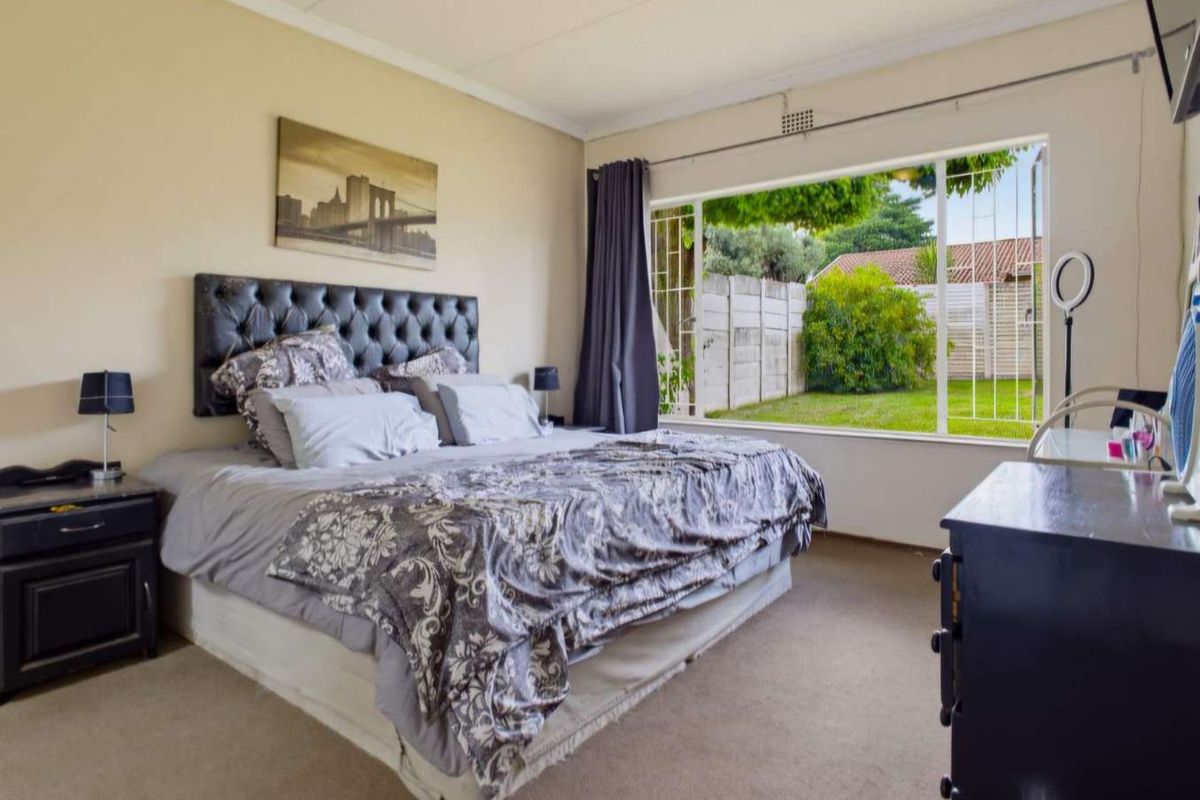 Spacious bedroom featuring large picture windows with security bars, neutral wall finishes, and carpeted flooring, offering a view of the rear garden.