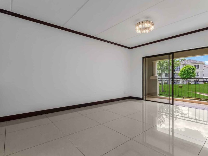 A bright, empty living room featuring large format floor tiles, dark crown molding, and a sliding glass door leading to a private balcony.
