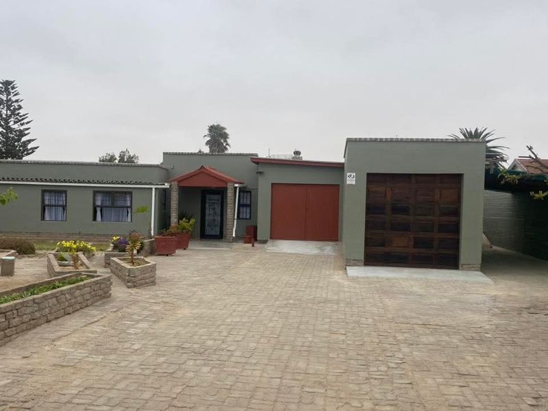 Front exterior view of a single-story house featuring a paved driveway, brick planter boxes, a wooden garage door, and a covered entrance.