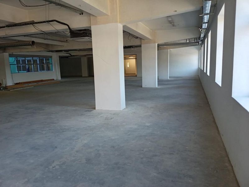 Spacious open-plan commercial interior featuring exposed concrete ceilings, structural columns, and industrial-style ducting, offering a versatile blank canvas for office or retail use.