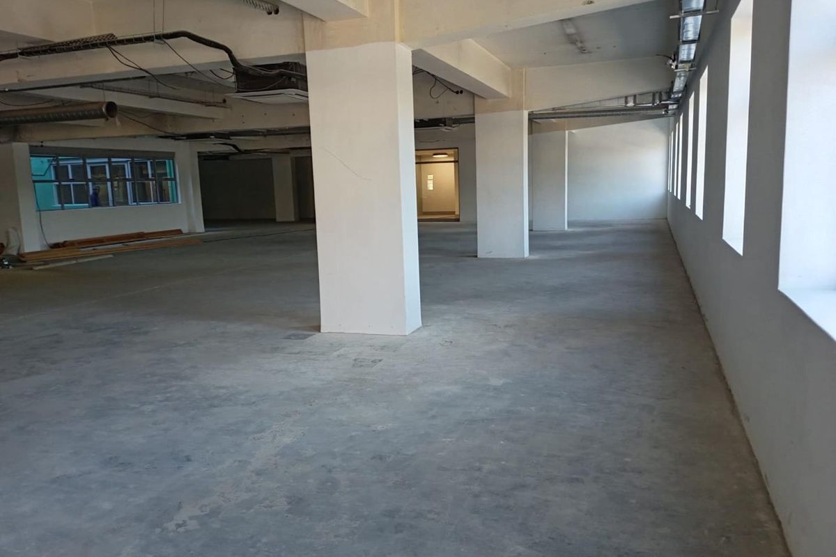 Spacious open-plan commercial interior featuring exposed concrete ceilings, structural columns, and industrial-style ducting, offering a versatile blank canvas for office or retail use.
