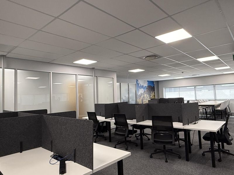 Modern open-plan office space featuring suspended ceilings, recessed LED lighting, glass partitions, and carpeted flooring, providing a professional and functional work environment.