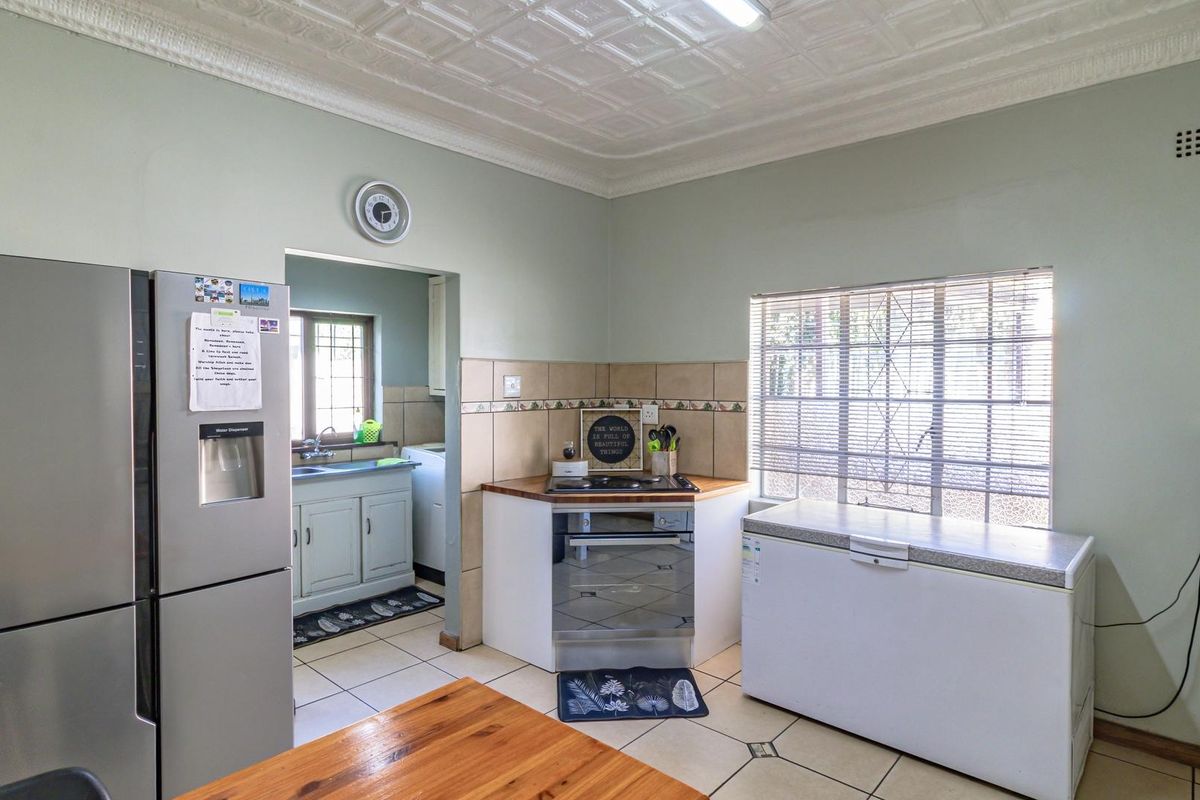 A functional kitchen featuring a built-in oven, hob, and tiled backsplash, with an adjoining scullery area and tiled flooring throughout.