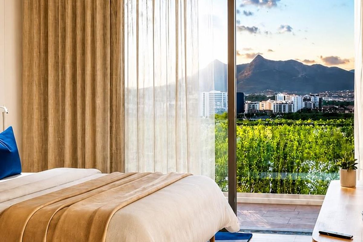 A bright bedroom featuring large sliding glass doors that open to a balcony with scenic mountain and city views.