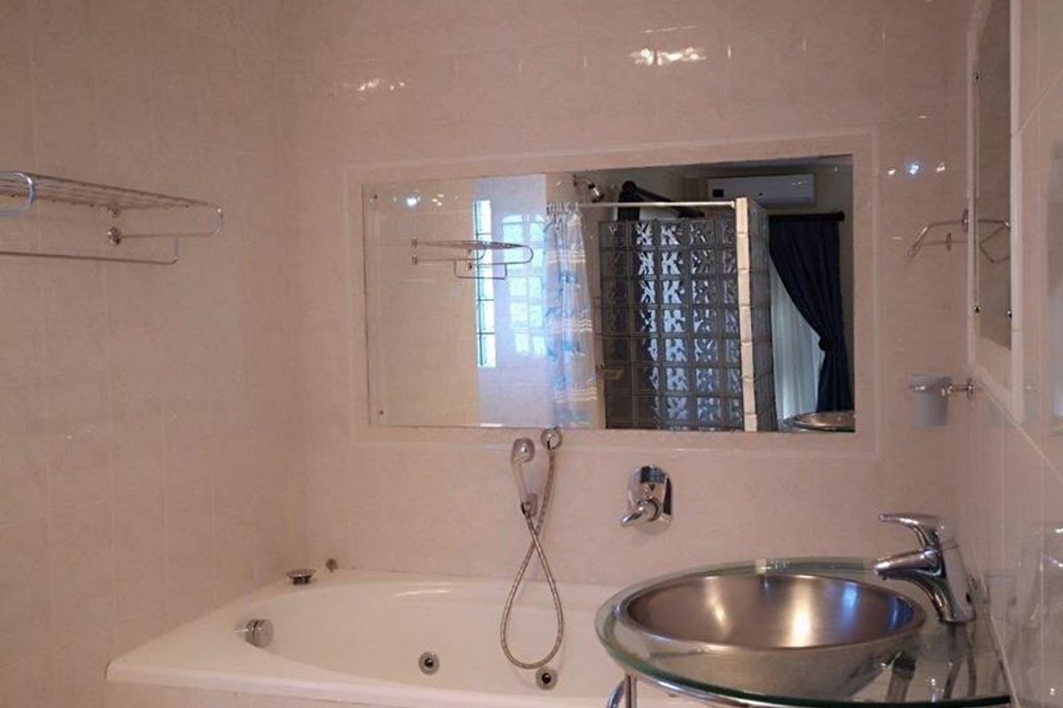 A functional bathroom featuring a built-in bathtub with shower mixer, a glass vessel sink vanity, and wall-mounted towel rails.