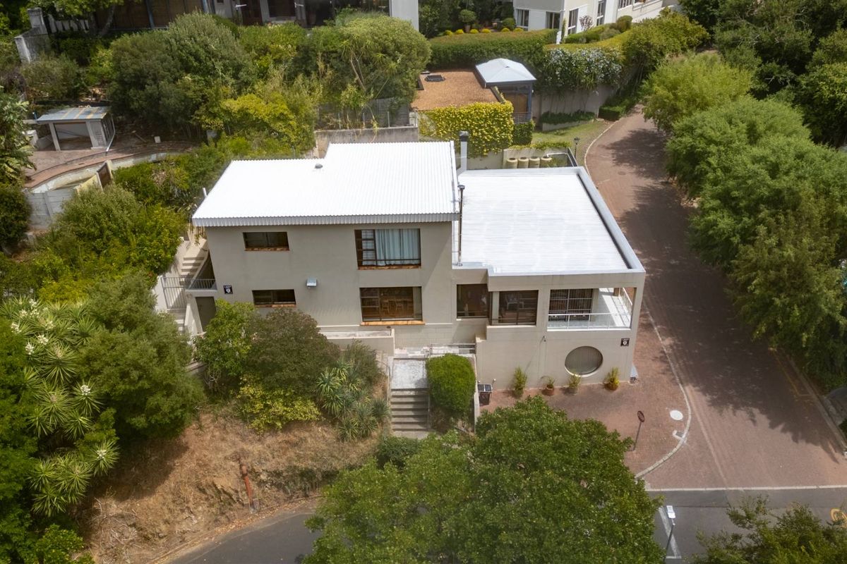 Aerial view of a multi-level residential property featuring a white corrugated metal roof, paved driveway, and established surrounding garden.