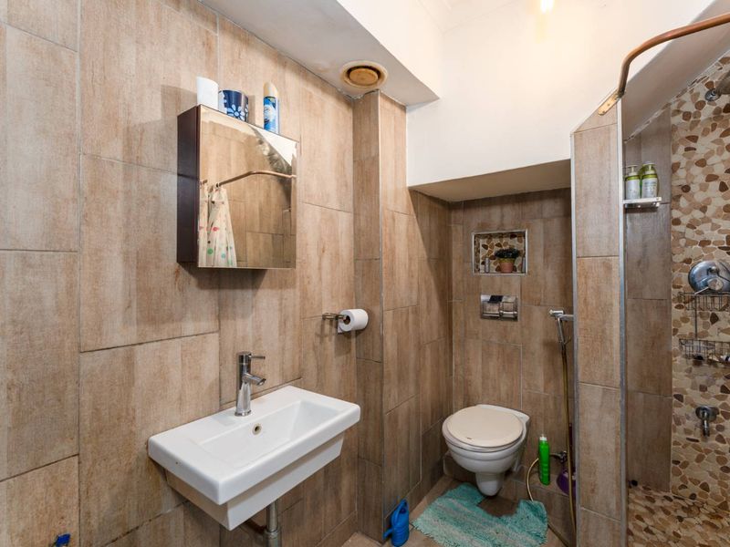 Compact bathroom featuring a wall-mounted basin, toilet with flush plate, and a shower area with pebble mosaic flooring and full-height wall tiling.