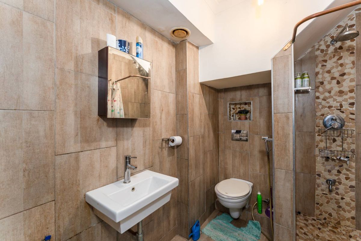 Compact bathroom featuring a wall-mounted basin, toilet with flush plate, and a shower area with pebble mosaic flooring and full-height wall tiling.