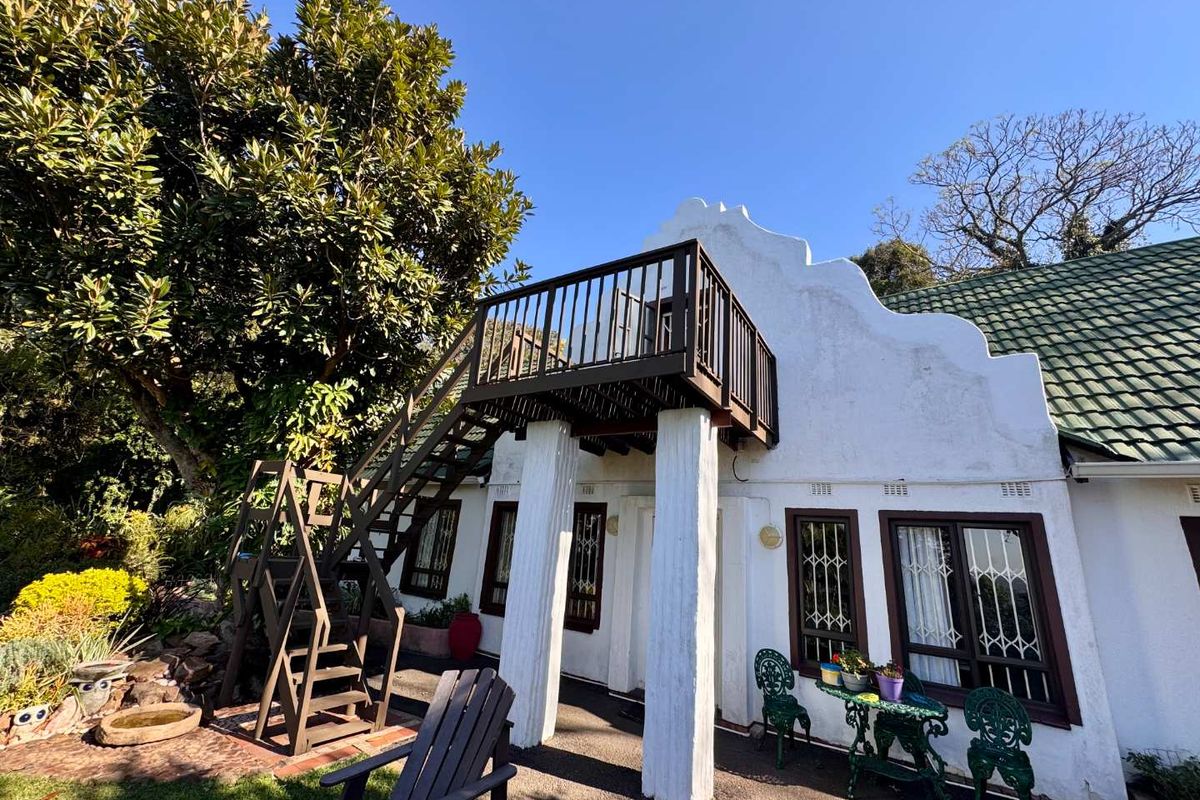A charming Cape Dutch style exterior featuring a raised wooden balcony with an external staircase, overlooking a private garden area.