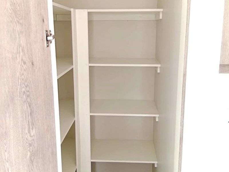 A clean, functional pantry or storage cupboard featuring white built-in shelving and wood-look cabinetry doors.