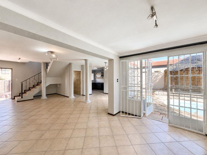 Spacious open-plan living area featuring ceramic tiled flooring, structural columns, and direct access to the pool area through sliding glass doors.