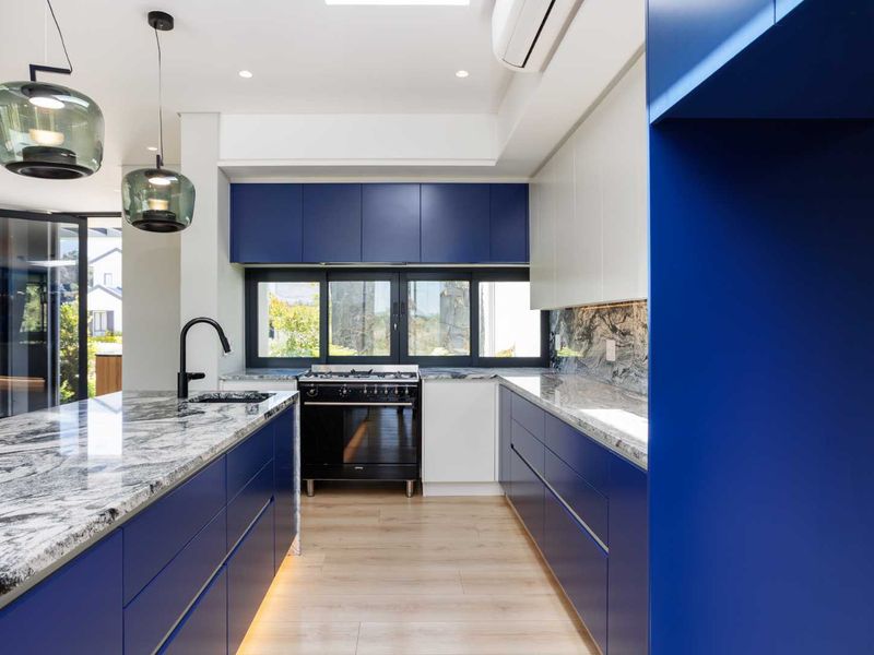 Modern kitchen featuring bold blue cabinetry, stone countertops, a central island, and high-end integrated appliances with sleek contemporary finishes.